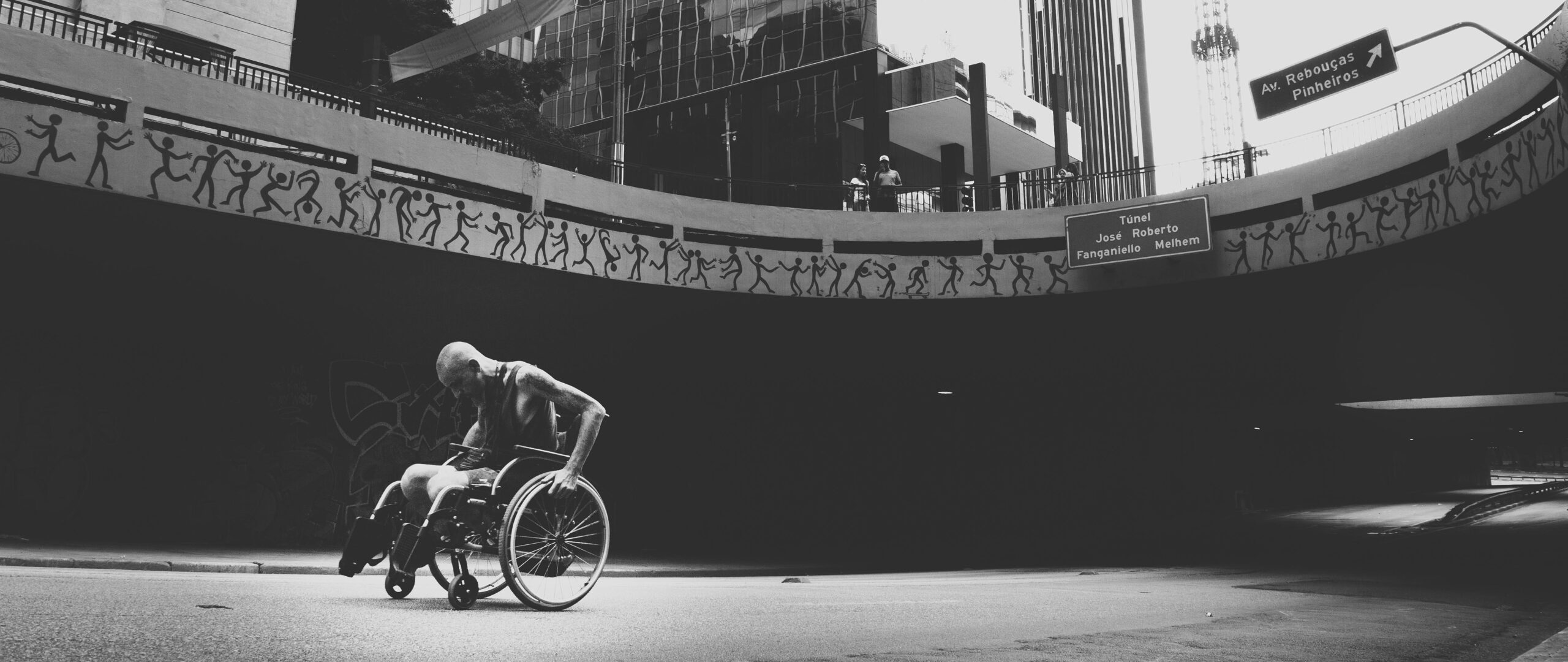 Black and white photo of a strong man in a wheelchair navigating a city street.